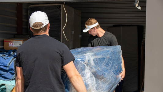 two Caddy Movers moving a wrapped piece of furniture into a storage unit