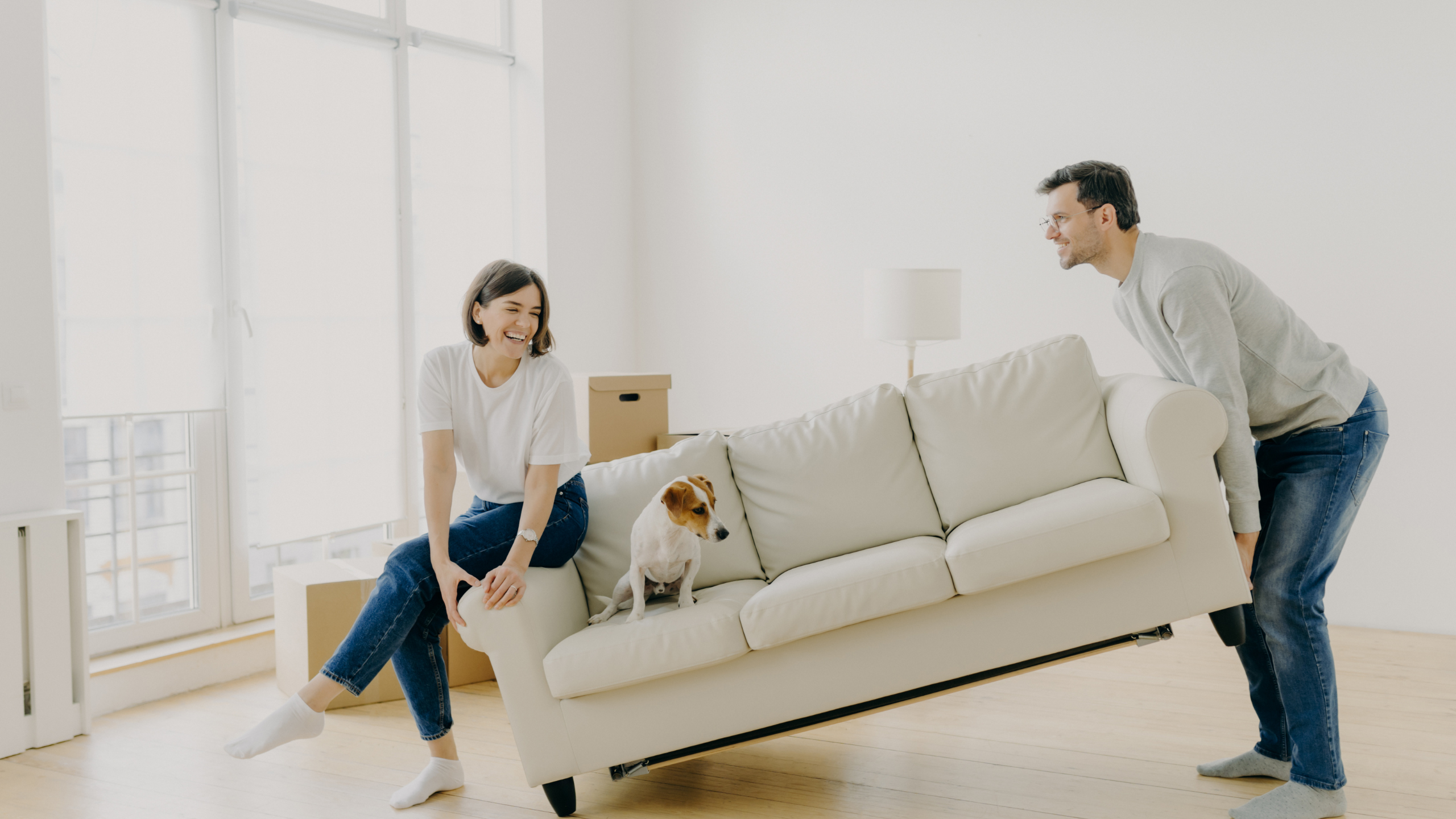 A family moving their white couch with a beagle sitting on the couch