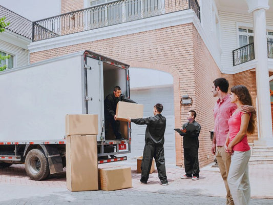 A moving company is loading boxes into a truck while a couple watches in front of their house.