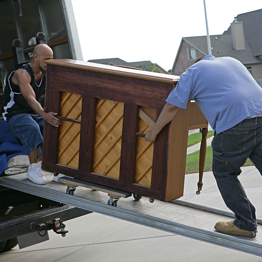 Two movers carefully maneuver an upright piano into a moving truck